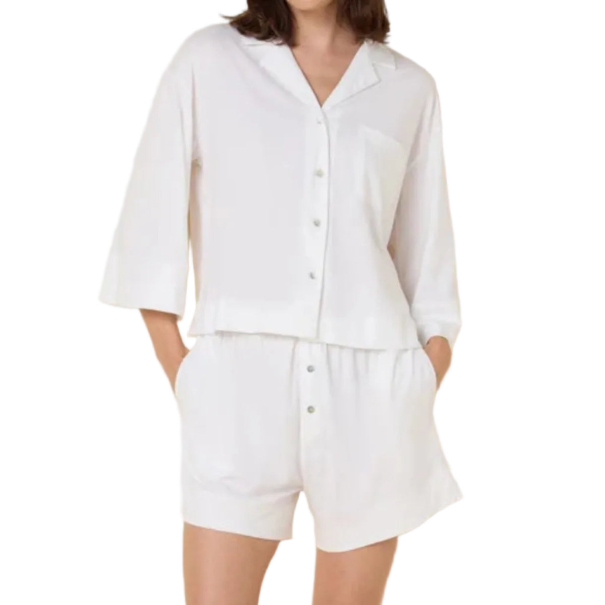 Woman wearing a white linen shirt and shorts set against a white background