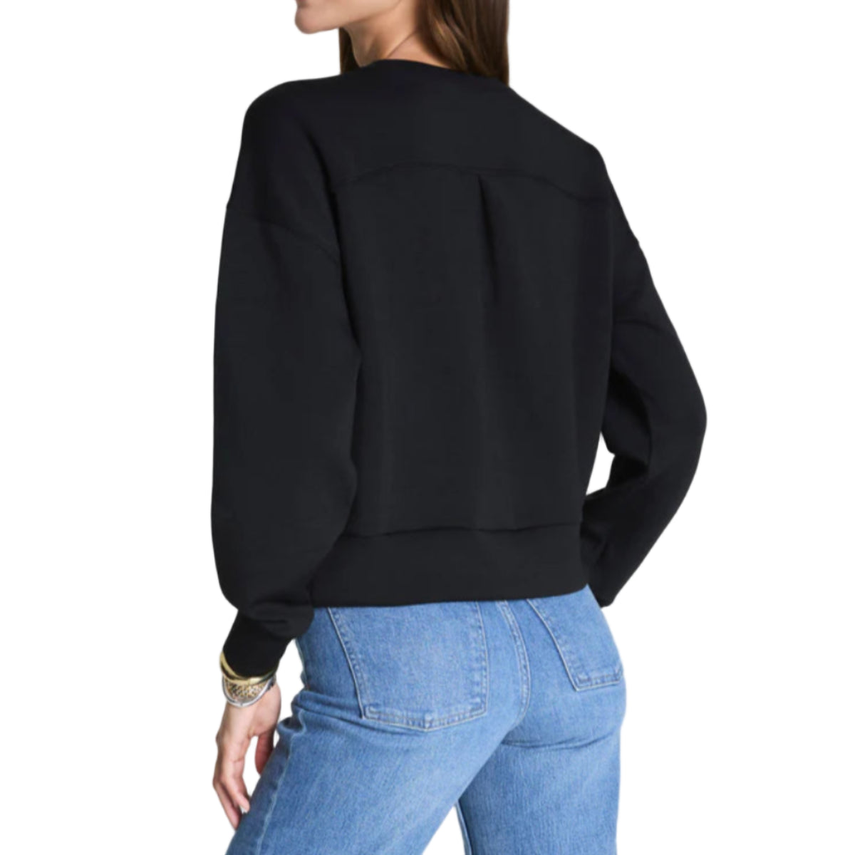 Woman wearing a black sweatshirt and blue jeans on a plain background