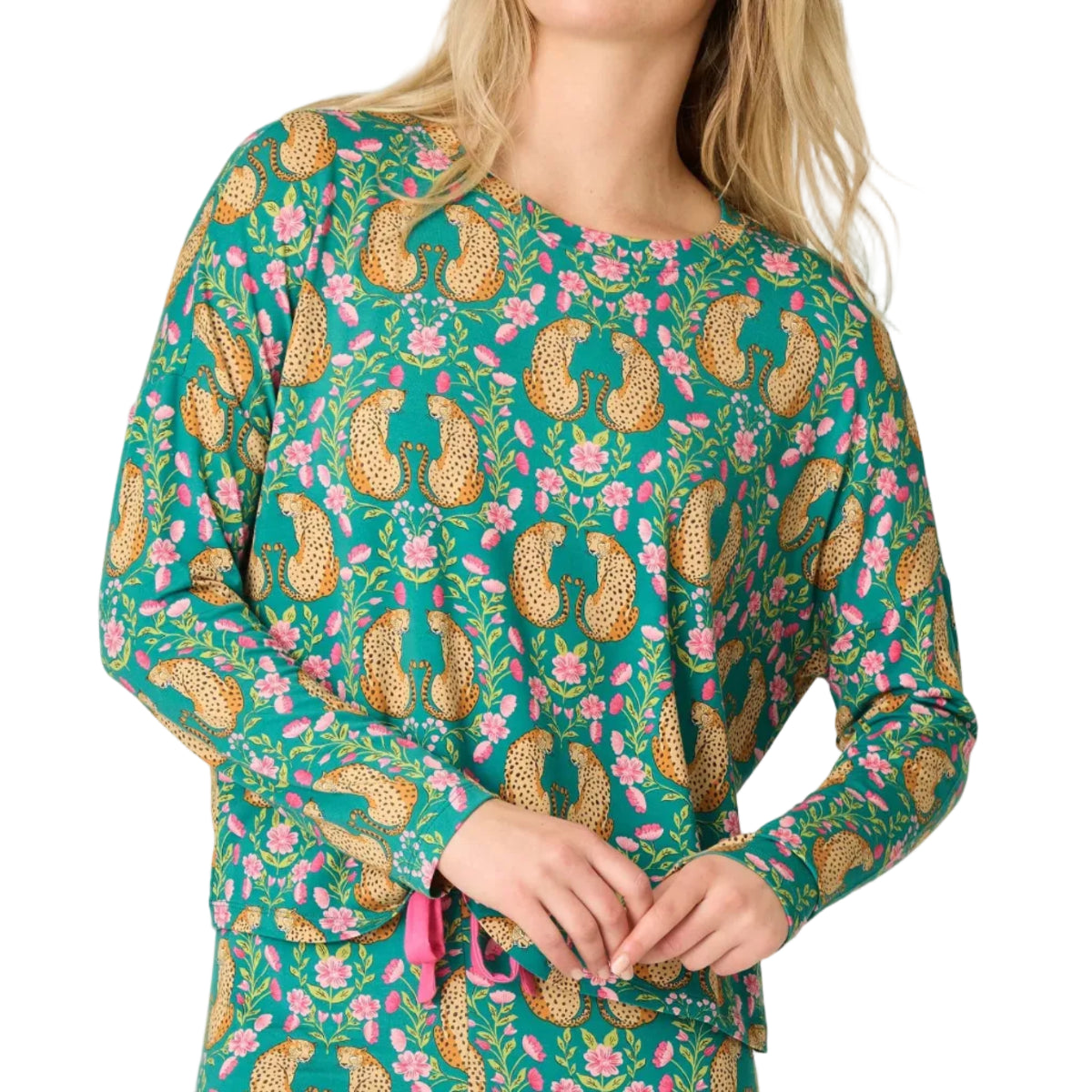 A woman wearing a long-sleeve pajama top with a green base and a colorful paisley and floral print, paired with matching pants, against a plain light background.