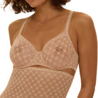 Woman wearing a beige lace lingerie set against a beige background