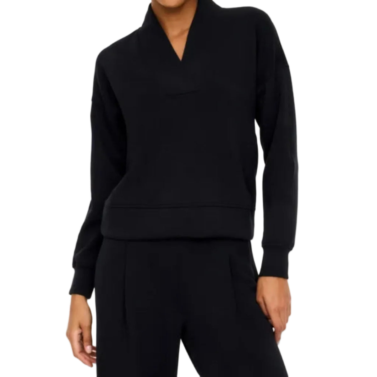 A model wearing a black long-sleeve top with a unique folded collar and matching black trousers, photographed against a solid off-white studio background.