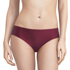 A model wearing a pair of low-rise, high-waisted bikini bottoms in a deep burgundy color, shown from the waist to the upper thighs against a light gray studio background.