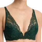 A close-up of a model wearing a dark forest green lace bra with scalloped edges and underwire, shown against a plain white background.
