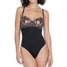 A woman modeling a black one-piece bodysuit with sheer black lace cups and thin shoulder straps, photographed against a plain light gray studio background.