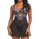 A woman modeling a sheer black babydoll lingerie bodysuit with a floral lace bust and waist panel in muted purple, green, and blue tones, against a plain white background.