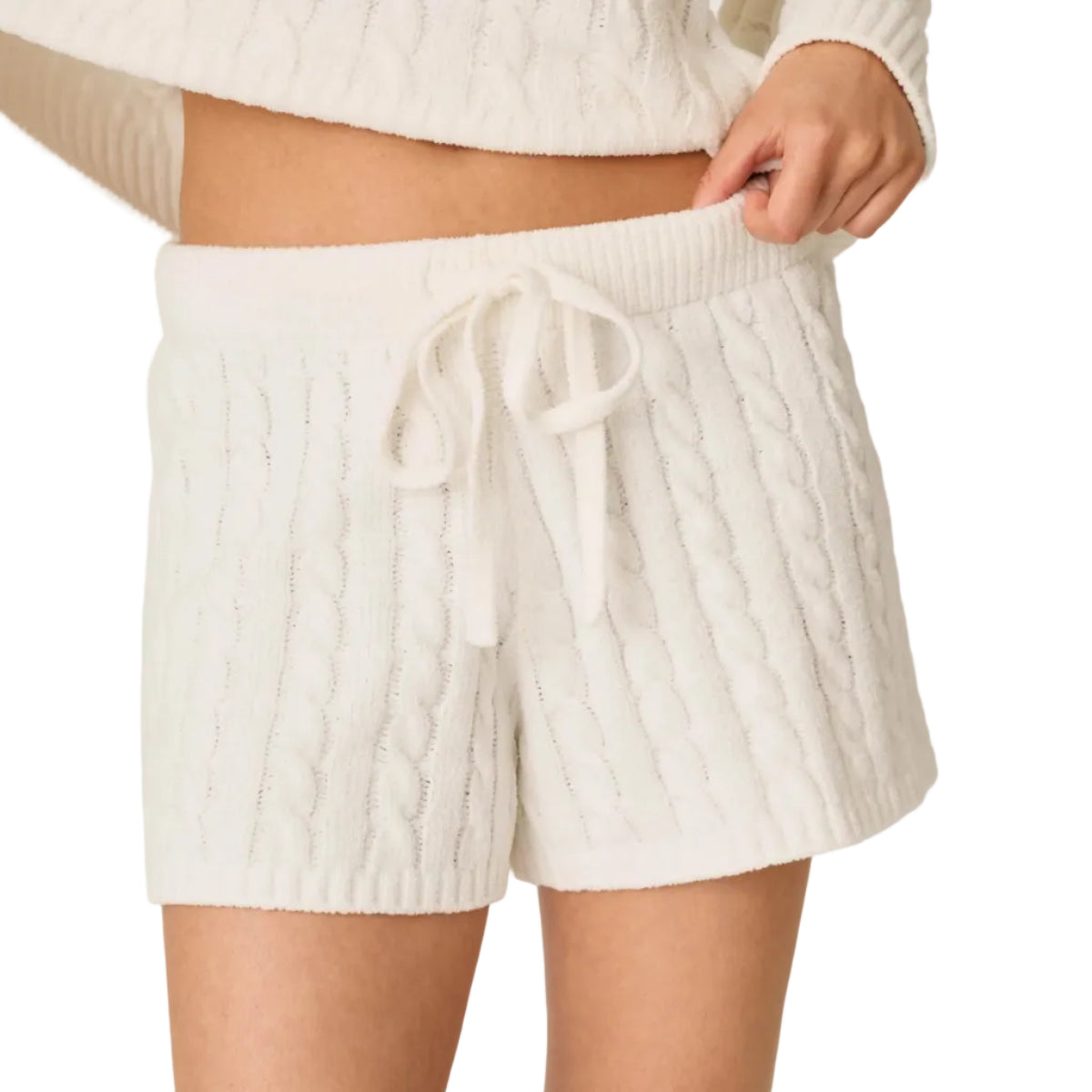 A person wearing cream cable-knit shorts with a matching drawstring waistband, paired with a cropped cream cable-knit sweater, shown against a plain light background.
