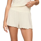 A model wearing cream-colored pleated shorts with a scalloped hem, paired with a matching cream top, shown from the waist down against a solid light beige background.