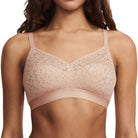 A woman modeling a light beige lace bralette against a plain white studio background.