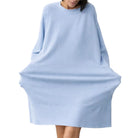 A woman wearing a light blue oversized long-sleeve knit top or poncho-style sweater, standing against a plain beige studio background.