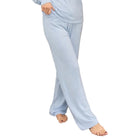 A woman wearing a light blue long-sleeve pajama set stands barefoot on a patterned rug in front of a rustic wooden door.