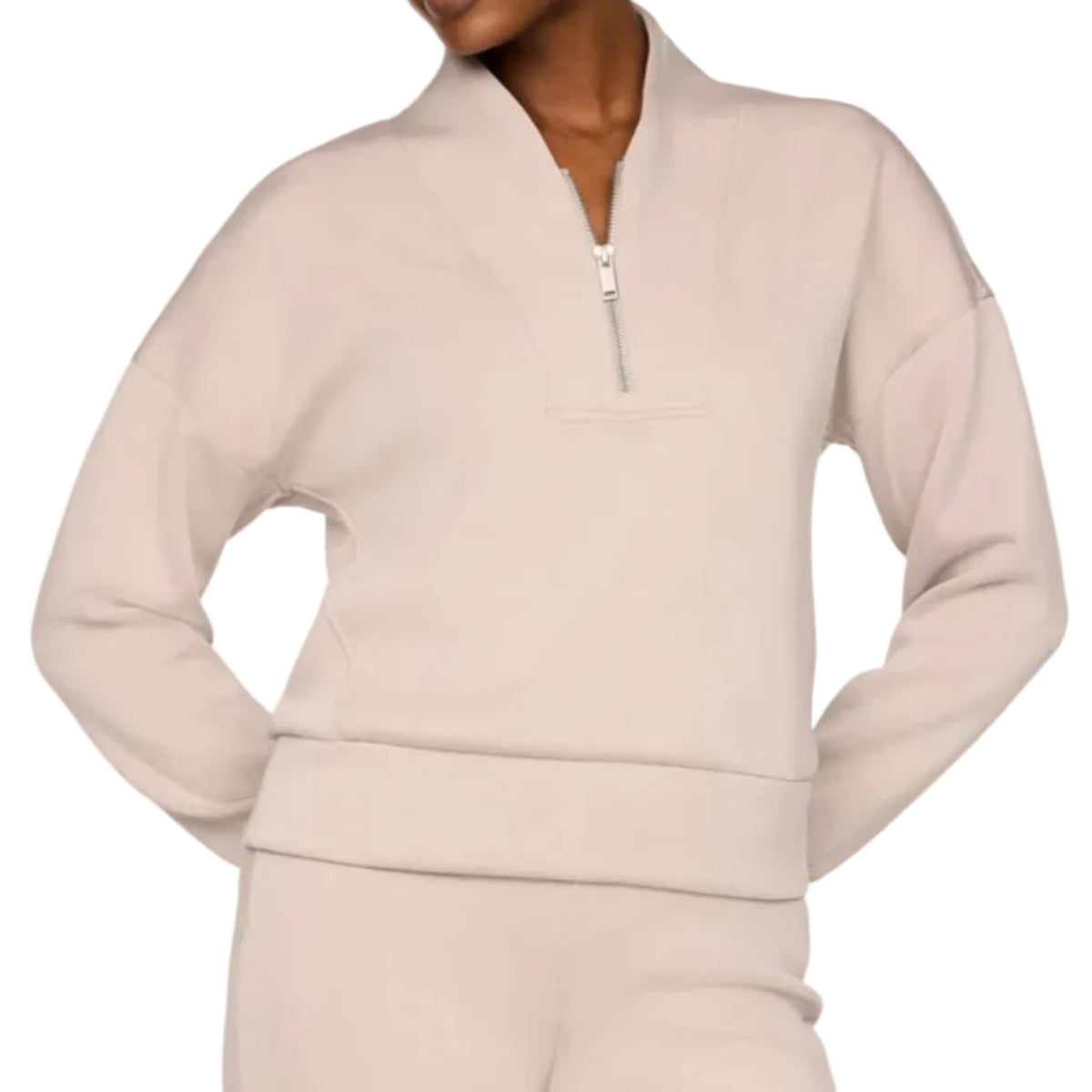 A model wearing a light beige matching lounge set consisting of a cropped quarter-zip sweatshirt and matching sweatpants, photographed against a solid off-white studio background.