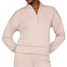 A model wearing a light beige matching lounge set consisting of a cropped quarter-zip sweatshirt and matching sweatpants, photographed against a solid off-white studio background.
