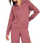 A woman modeling a dusty rose half-zip pullover sweatshirt with matching sweatpants against a solid off-white background.