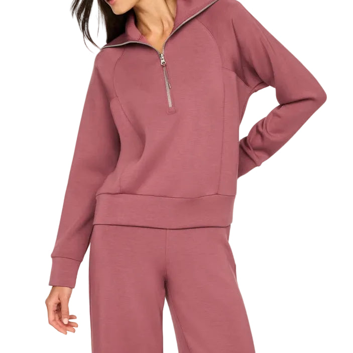 A woman modeling a dusty rose half-zip pullover sweatshirt with matching sweatpants against a solid off-white background.