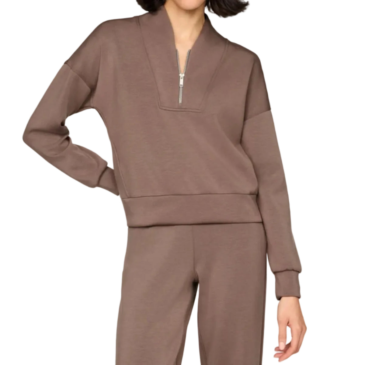 A woman modeling a matching taupe-brown lounge set consisting of a long-sleeve half-zip sweatshirt and coordinating sweatpants, shot against a solid light beige background.