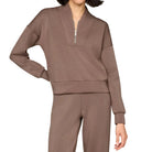 A woman modeling a matching taupe-brown lounge set consisting of a long-sleeve half-zip sweatshirt and coordinating sweatpants, shot against a solid light beige background.
